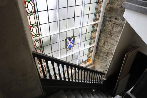 Image of mostly clear, partially stained glass window by a staircase at St John's