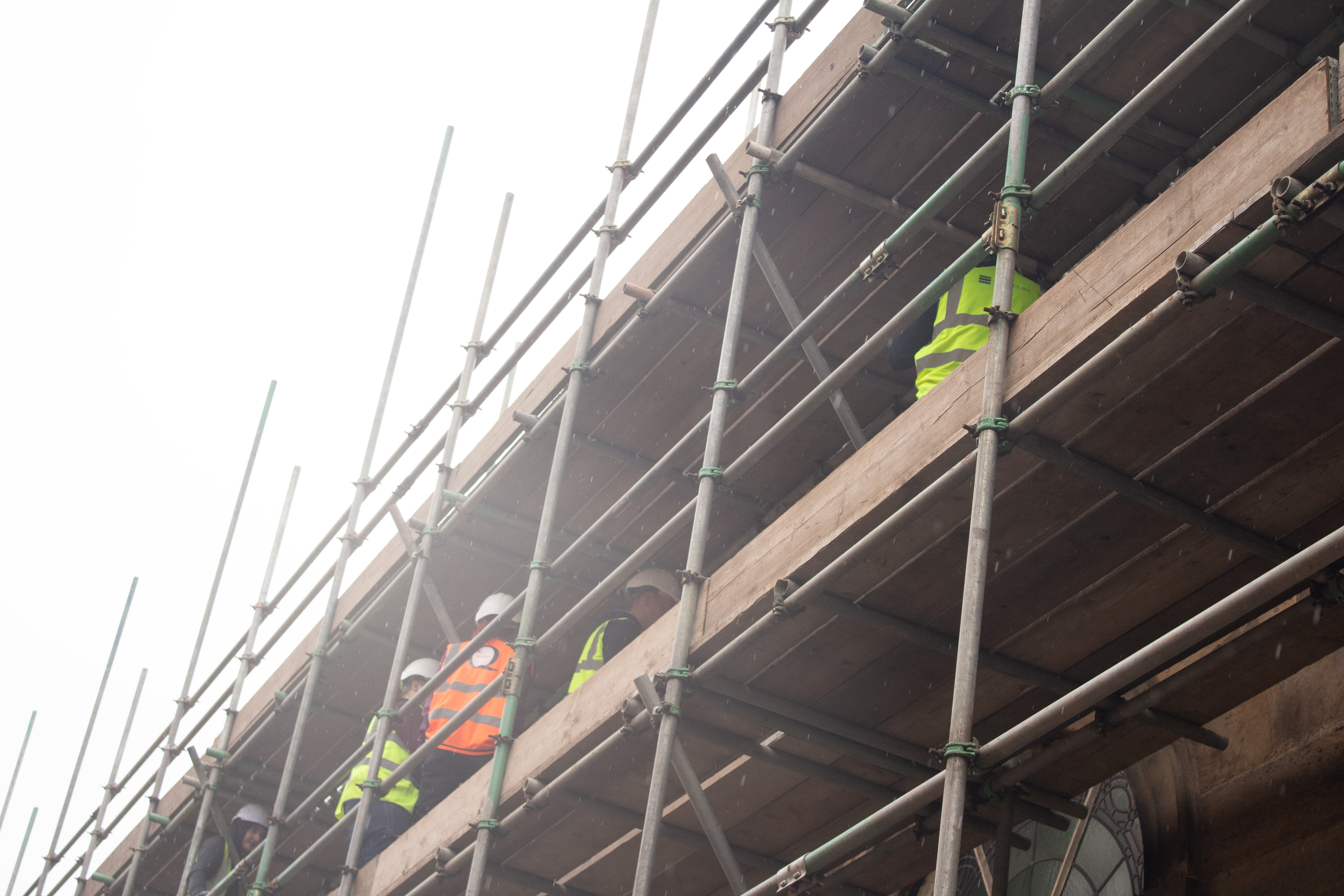 Apprentices in hi-vis jackets and hard hats on high up scaffolding in the rain.